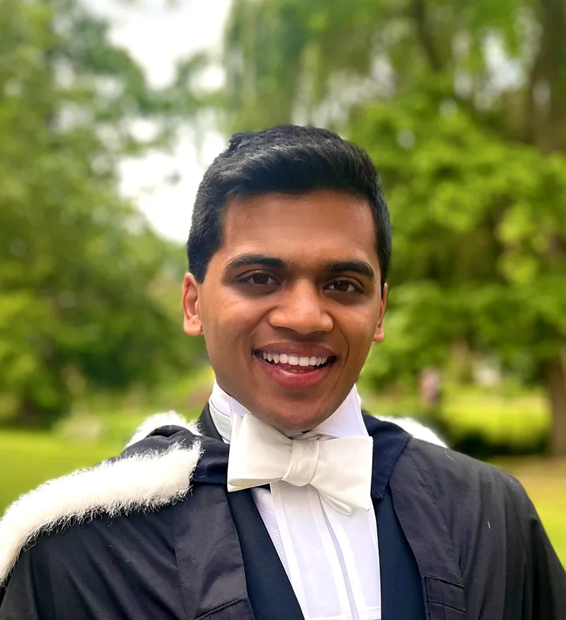 Neil Sardesai smiling outdoors in Cambridge academic dress with a white bow tie